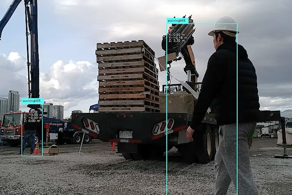 Computer screen display of a smart construction site, where workers are detected within a construction zone and the level of danger indicated by a blue box and percentage of danger around them.
