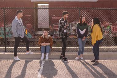 Five youth standing in front of a school barbed wire fence and talking to each other