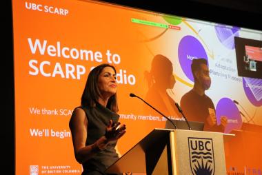 Woman speaking at lectern in front of "Welcome to SCARP Studio" sign