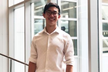 UBC ECE student Tony Xu smiles at the camera. He is centred with windows behind him.