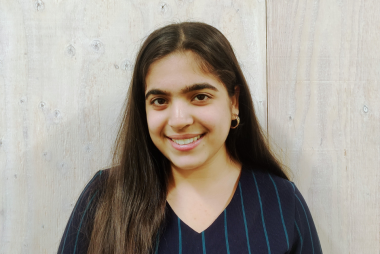 Janavi, smiling in front of the camera while standing in front of a white wall