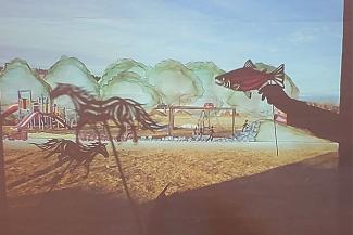 An illustration of horses running in a field with a fish in the foreground is projected onto a wall.