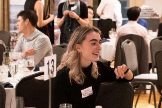 Lucy Myrol is centered, smiling while looking to the right. She is seated in a banquet hall during an event.