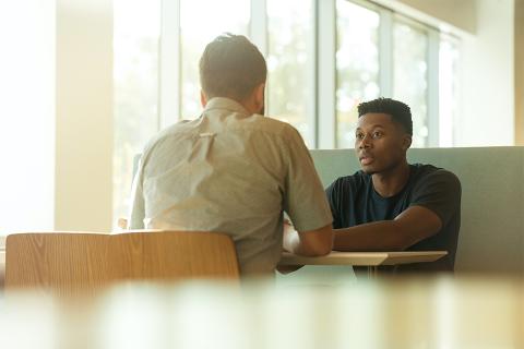 Two men are seated at a table across from one another, clearly engaged in deep conversation