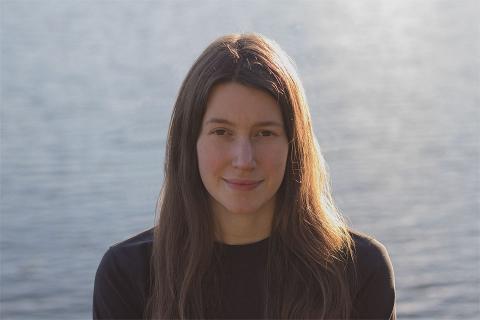 UBC SALA student Isla Francis smiles at the camera. She is centred with the ocean behind her.